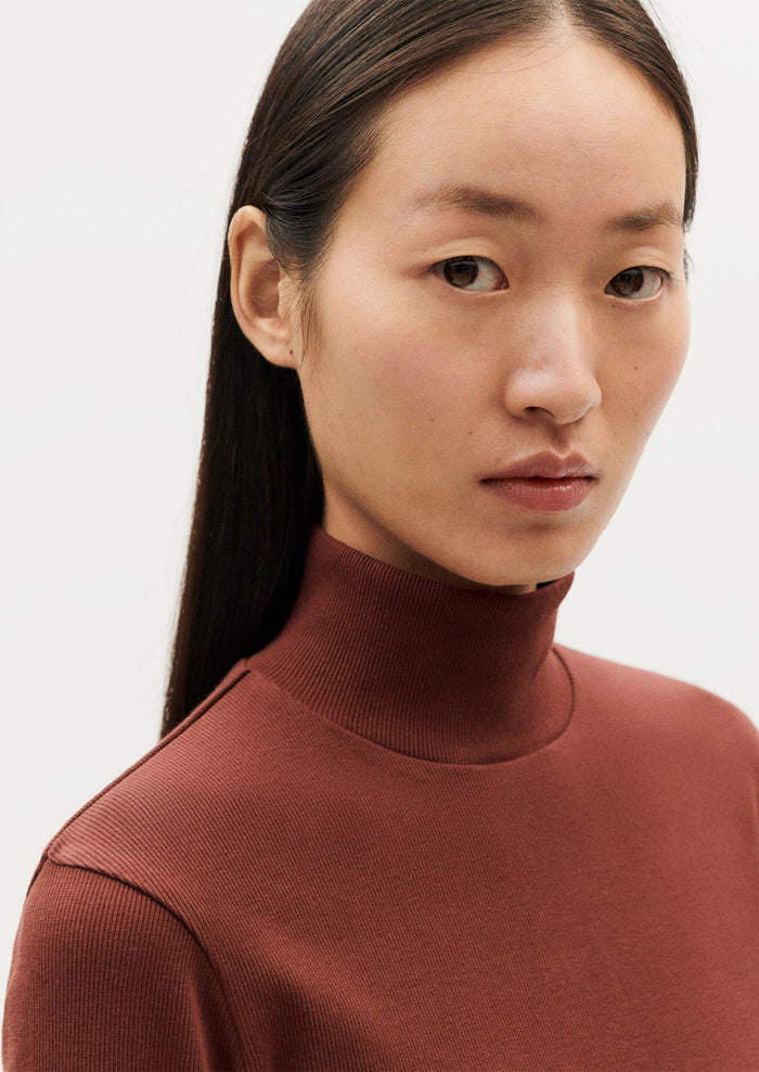 A woman wearing a form fitting, long sleeve turtleneck t-shirt in brown.