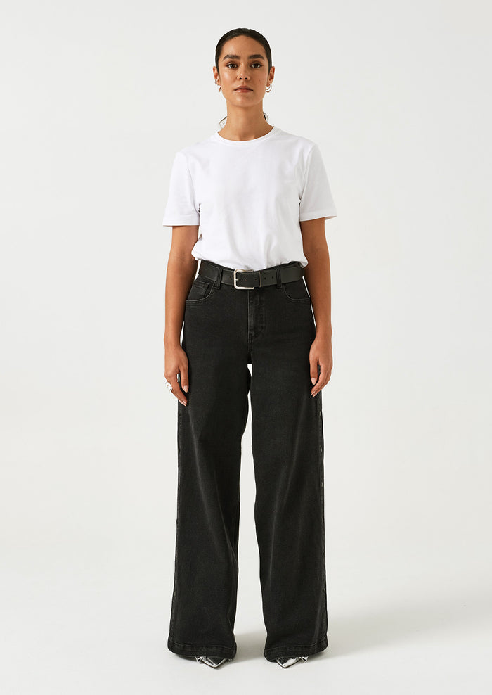 A woman wearing a pair of black wide leg jeans with windbreaker-style snap detail along outer leg.