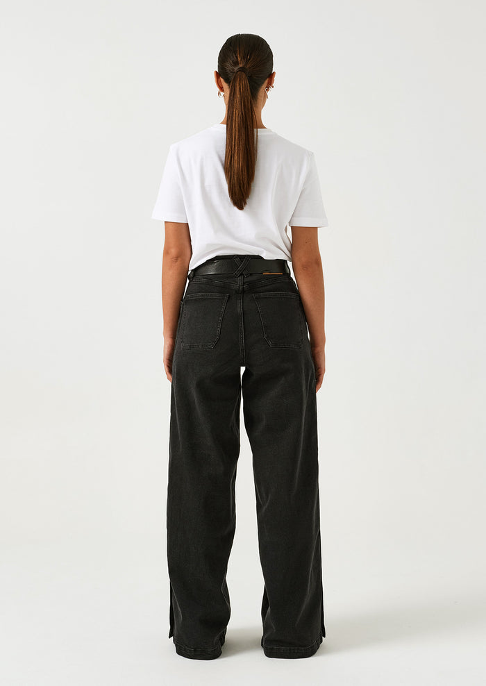 A woman wearing a pair of black wide leg jeans with windbreaker-style snap detail along outer leg.