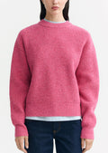 A woman wearing a chunky knit sweater in pink color.