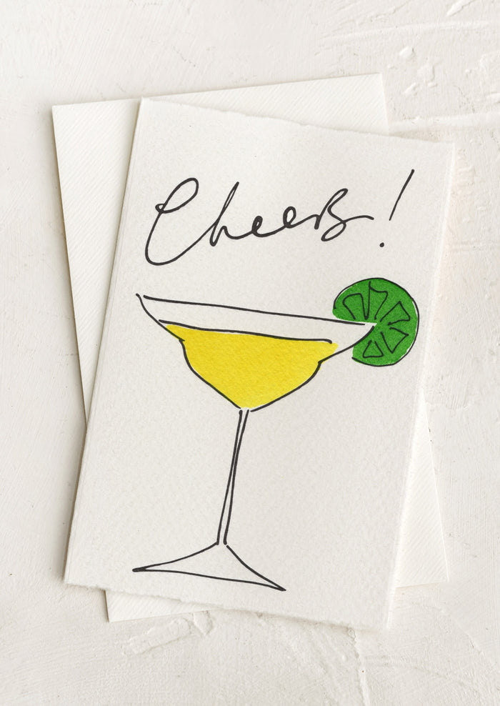 A greeting card with hand painted illustration of a martini, text above reads "Cheers!".