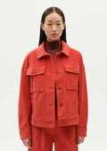 A woman wearing a shirt jacket style corduroy long sleeve jacket in red-orange hue.