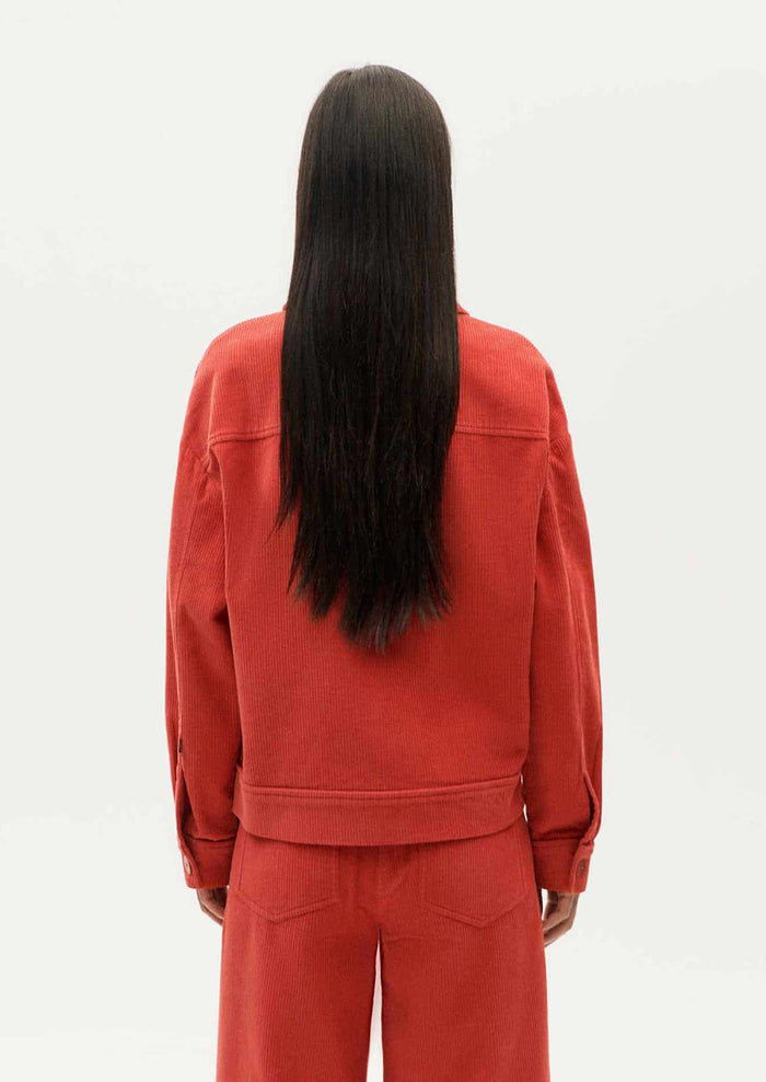 A woman wearing a shirt jacket style corduroy long sleeve jacket in red-orange hue.