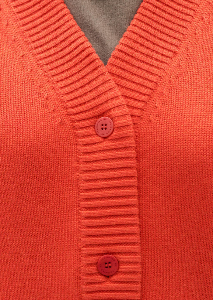 A woman wearing a button front, long sleeve cardigan sweater in red-orange huge.