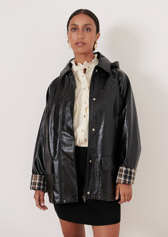 A woman wearing a patent jacket in black with plaid lining.